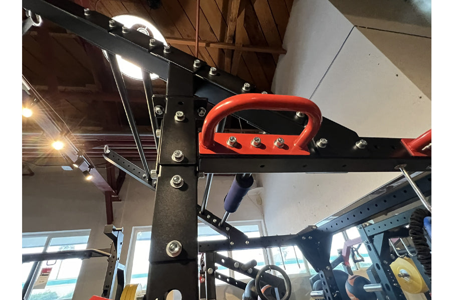 Black and red steel power cage with integrated weight plate storage, red carabiner handles, and silver bolts throughout, disp