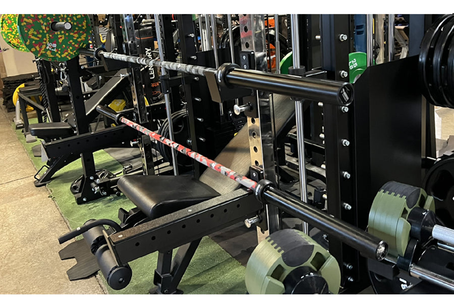 Warrior 6-bearing barbell with red camo cerakote coating and chrome sleeves, displayed on squat rack in gym setting