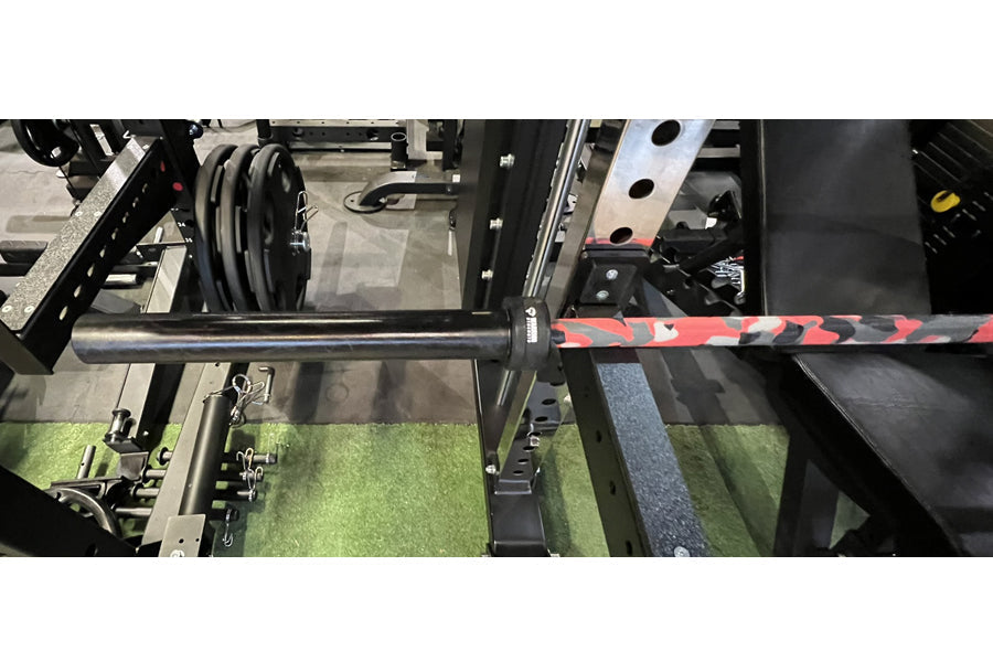 Warrior 6-bearing barbell with black cerakote shaft and red camo sleeve collars, shown on rack