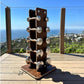 Dark wood dumbbell tower with stainless steel handles holding five pairs of weights, displayed on wooden deck with ocean view