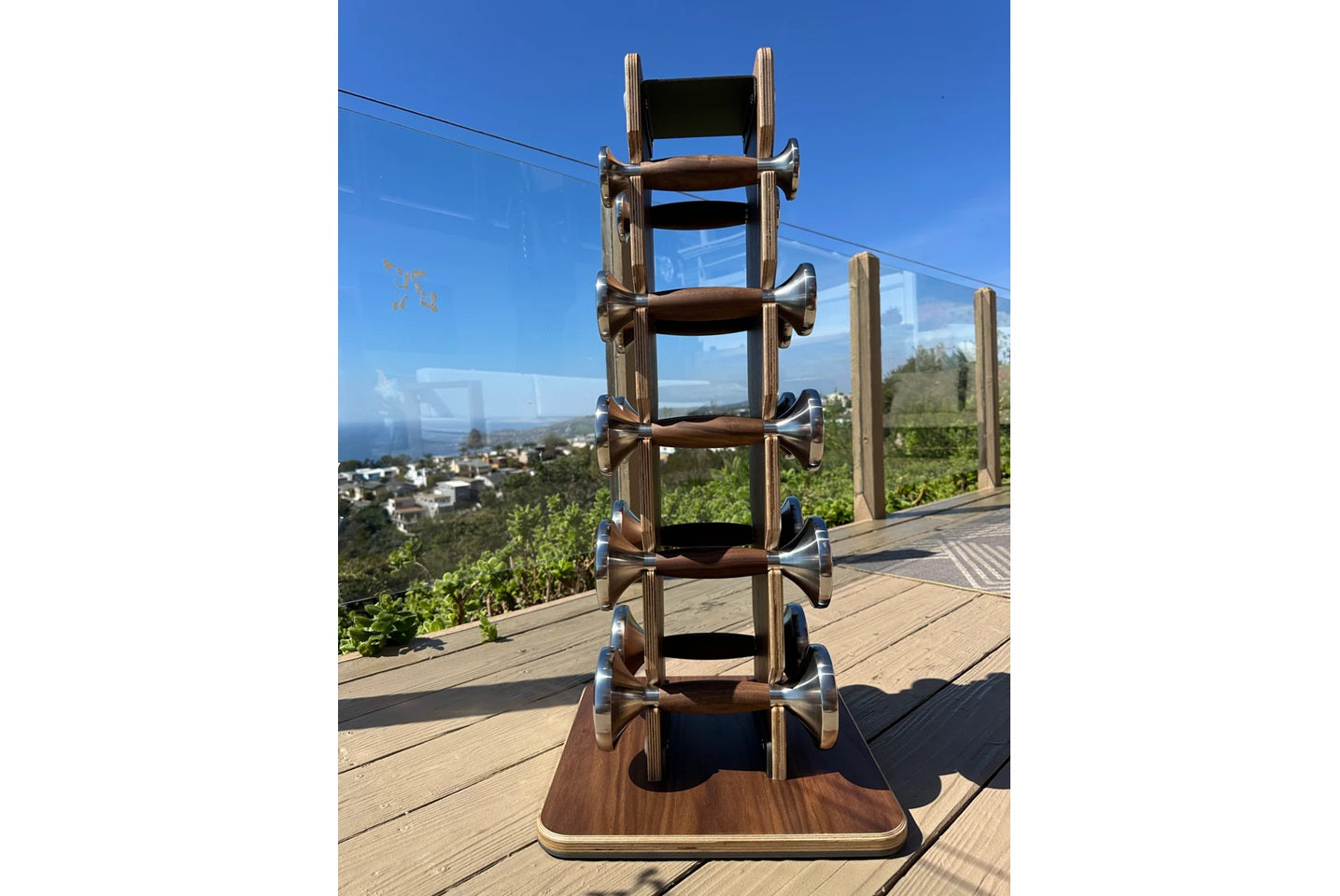 Warrior Luxury Wood dumbbell set with stainless steel handles displayed vertically on wooden base, outdoors on deck