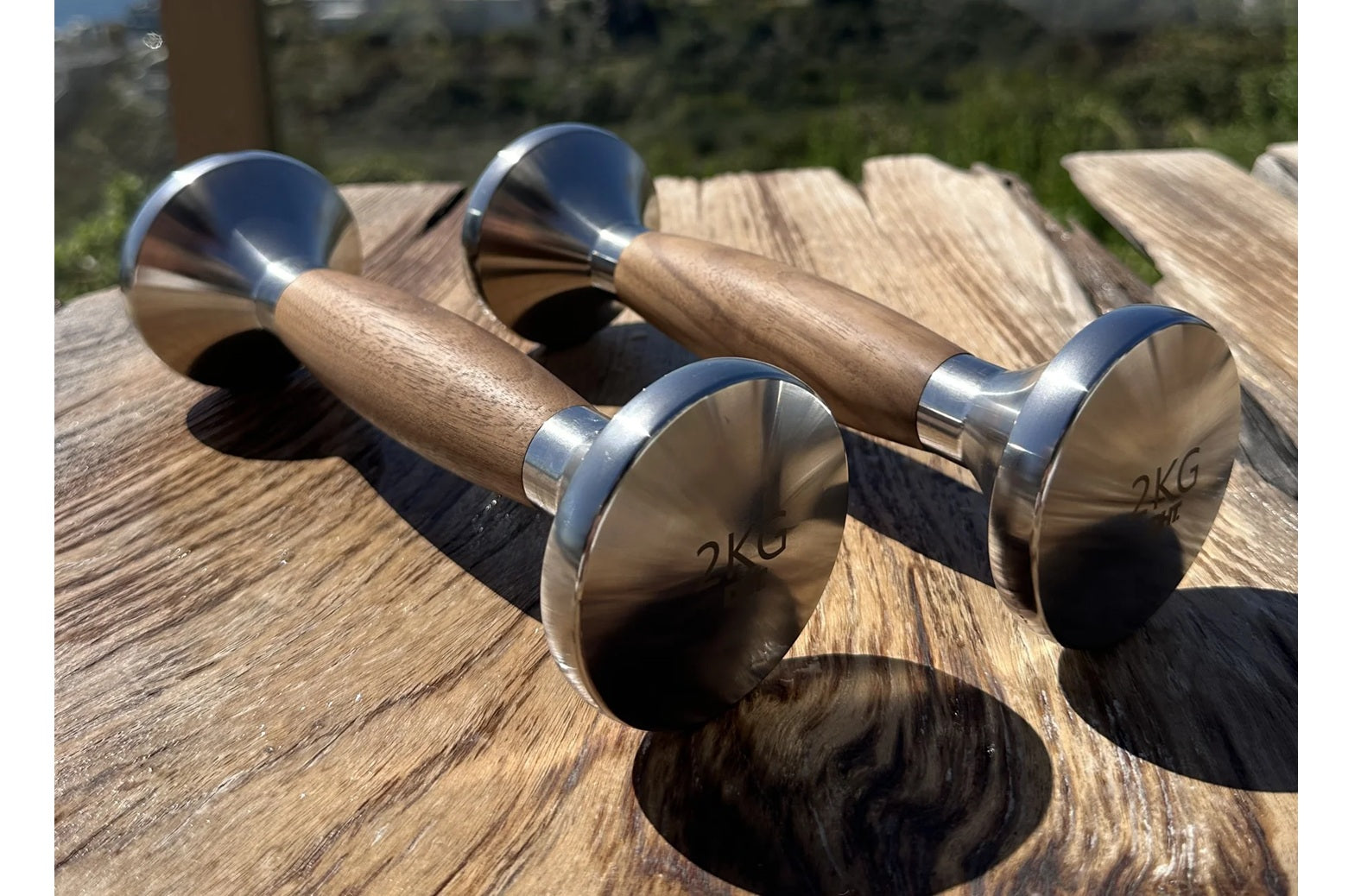 Pair of 2kg stainless steel dumbbells with natural wood handles on wooden deck