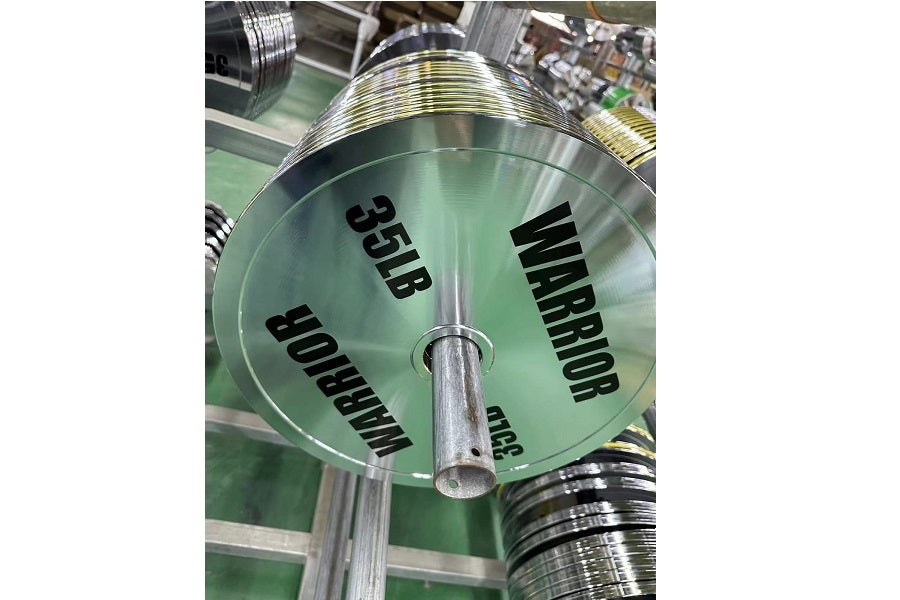 Warrior 25lb chrome Olympic weight plate with black text on green background, displayed on pole in gym setting