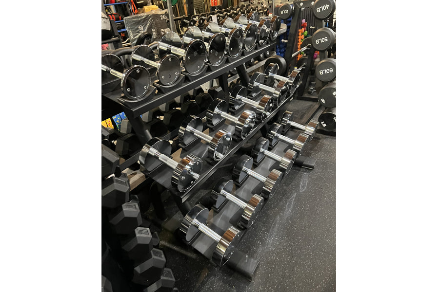 Warrior Pro-Style chrome dumbbell set arranged on black rack in gym, ranging from 5 to 50 pounds with numbered weights visibl