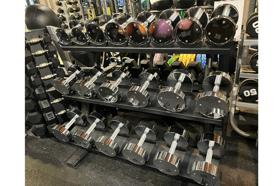 Warrior Pro-Style Chrome Dumbbell Set displayed on black tiered rack in gym, featuring chrome handles with black and colored 