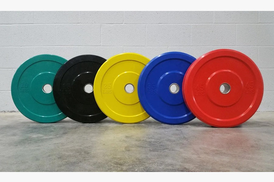 Five Olympic bumper plates in teal, black, yellow, blue, and red with chrome center hubs, displayed on concrete floor
