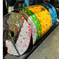 Colorful rubber bumper plates with fleck pattern in red, yellow, green, and blue, stacked and displayed on black rack