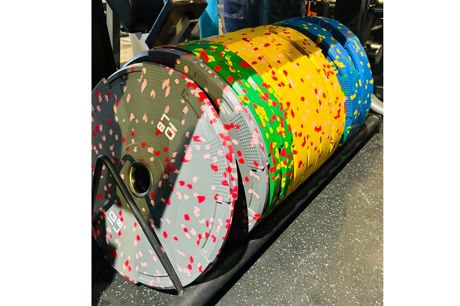Colorful rubber bumper plates with fleck pattern in red, yellow, green, and blue, stacked and displayed on black rack