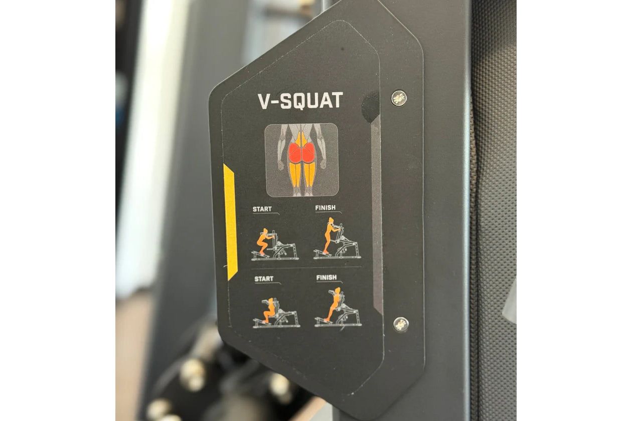 Black V-Squat machine instruction plate showing muscle target areas and exercise form with orange and red anatomical illustra
