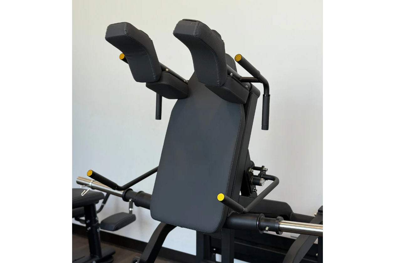 Black padded V-squat machine with dual padded shoulder supports, yellow adjustment knobs, and black metal frame on white back