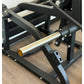 Black metal V-squat machine with polished chrome bar, padded shoulder rest, and adjustable seat on wooden floor