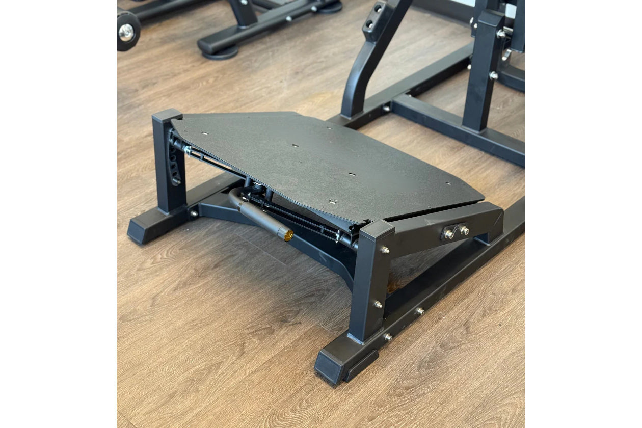 Black V-squat machine with gray cushioned platform, adjustable backrest, and metal frame on wooden gym floor