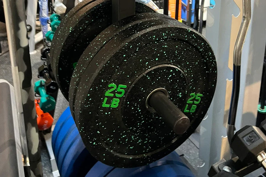Black speckled bumper plate with green 25 LB markings, loaded on barbell in gym setting