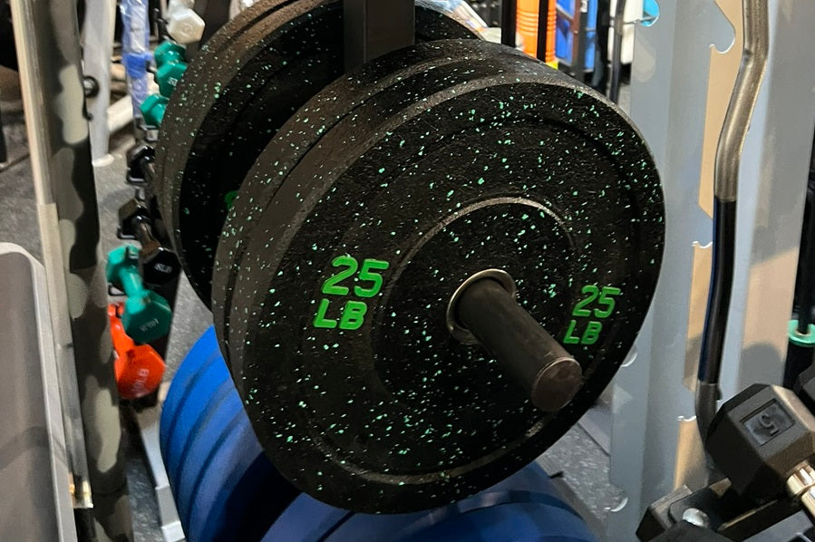 Black speckled rubber bumper plate with green "25 LB" markings, stacked on weight rack