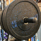 45 lb black rubber bumper plate with blue speckle and text, mounted on barbell in gym setting
