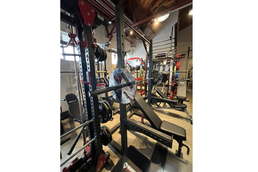 Warrior Deluxe Squat Rack with blue weight plate and black barbell in gym setting
