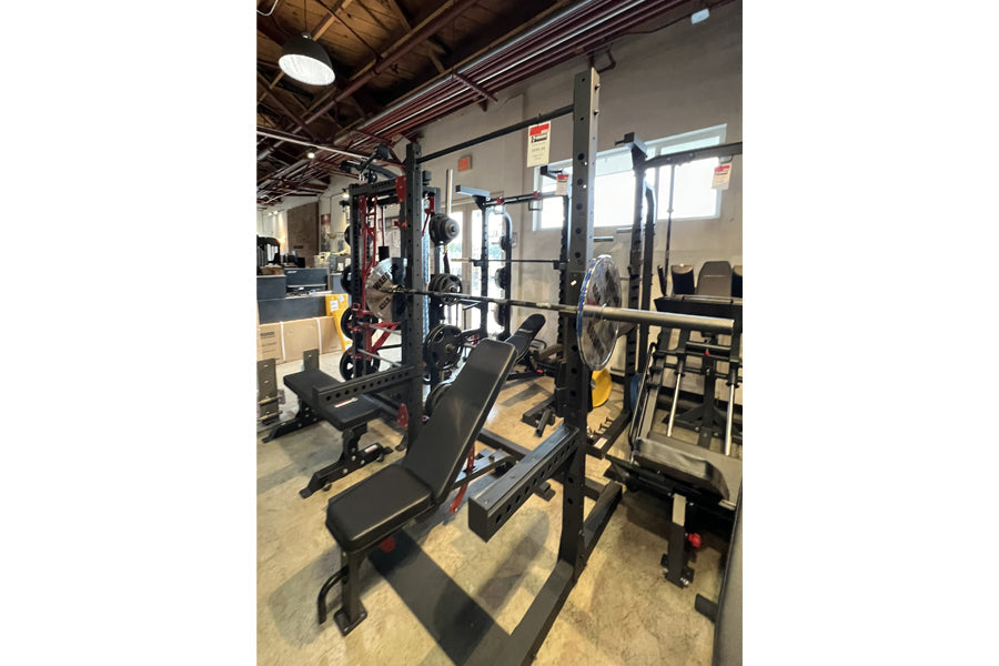 Warrior Deluxe Squat Rack with black uprights, weight plate storage, and adjustable safety bars in gym setting