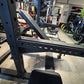 Black steel squat rack with angled uprights and perforated safety bars, shown in warehouse setting