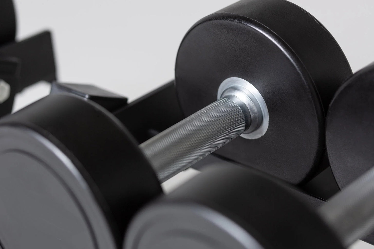 Black urethane dumbbell with textured gray grip and chrome collar detail, displayed among other dumbbells on white background