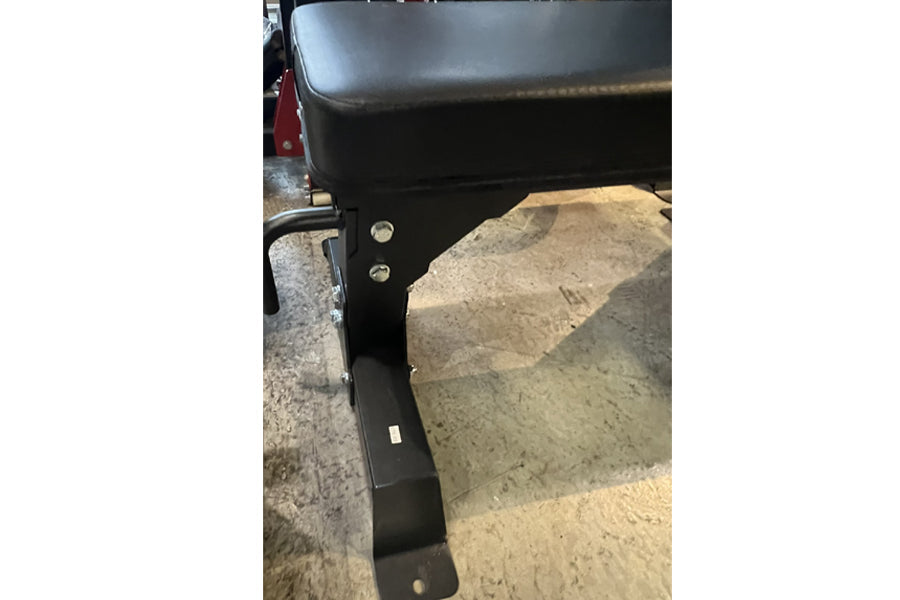 Black flat weight bench with wheels and metal rivets, side view on concrete surface