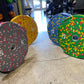 Colorful bumper plates with speckled rubber coating displayed on gym floor, including gray with red flecks, yellow with red f