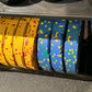 Colorful rubber bumper plates arranged in row showing yellow plates with red and pink flecks, blue plates with yellow and gre