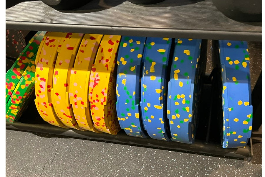 Colorful rubber bumper plates arranged in row showing yellow plates with red and pink flecks, blue plates with yellow and gre