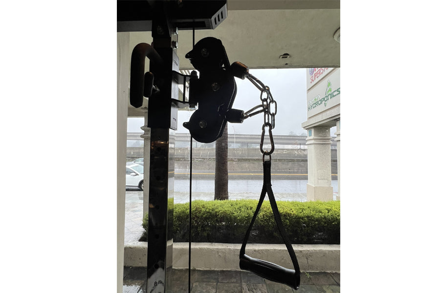 Black cable pulley functional trainer with chain attachment mounted on pole, shown in gym setting with waterfront view