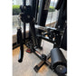 Black multi-functional home gym machine with leg press attachment, pulleys, and weight stack components in indoor setting