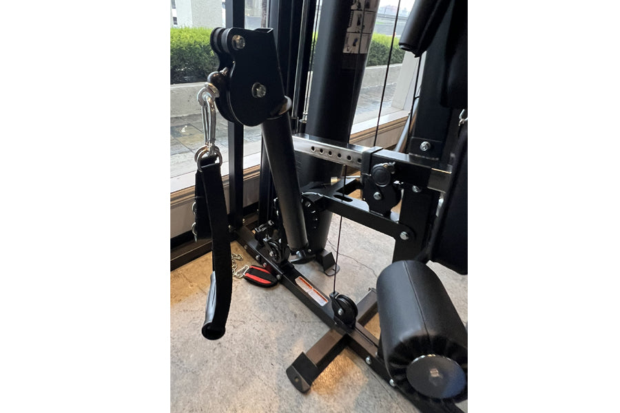 Black multi-functional home gym machine with leg press attachment, pulleys, and weight stack components in indoor setting