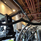 Black and silver home gym equipment with curved handlebars, leg press attachment, and cable pulley system in gym setting