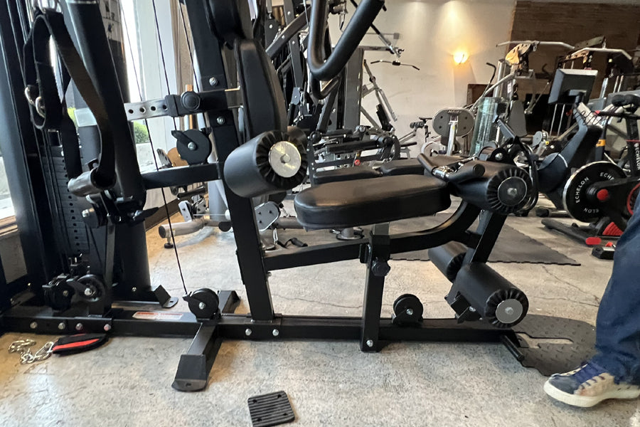 Black home gym equipment with leg press attachment and adjustable weight stack in gym facility setting