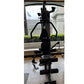 Black home gym equipment with curved handles, seat, and leg press attachment, photographed indoors by window