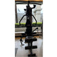 Black multi-station home gym with leg press attachment, pull-down cable system, and foot pedals, viewed from front in indoor 