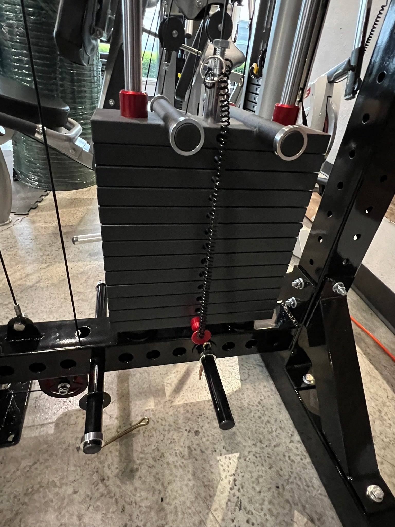 Black metal lat pulldown and low-row home gym system with stacked weight plates, chrome handles, red accents, and chain attac
