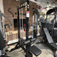 Black steel lat pulldown and low-row home gym system with white overhead bar, red weight pins, and black padded seat, display