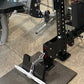 Black metal lat pulldown and low-row machine with perforated steel frame, red accents, and white foot plate on gym floor