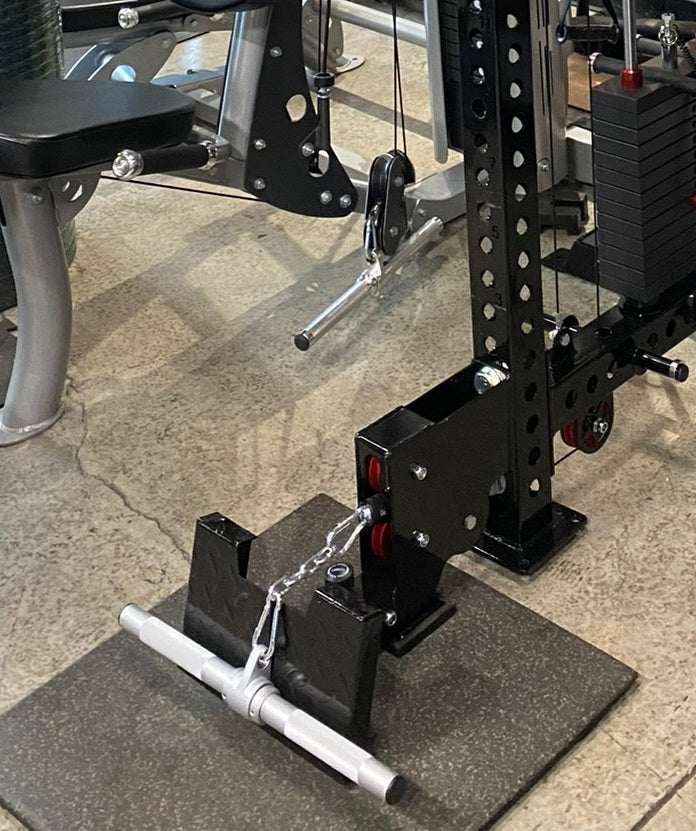 Black metal lat pulldown and low-row machine with perforated steel frame, red accents, and white foot plate on gym floor