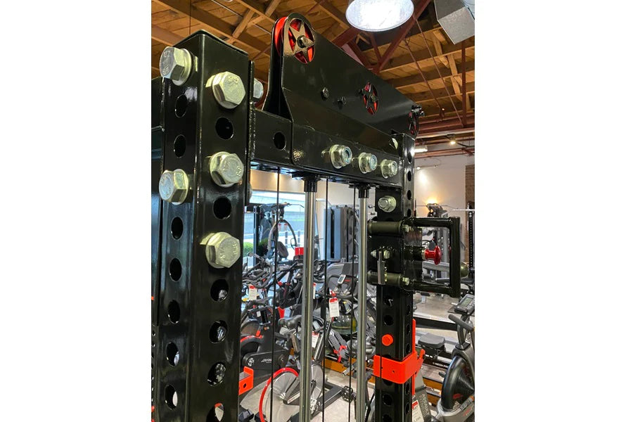Black steel cable crossover machine with glass doors, multiple brass pulleys, and red accents, displayed in gym setting