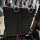 Black rubber stacked weight plate storage attachment with silver metal handles and red safety pins, mounted on gym equipment 