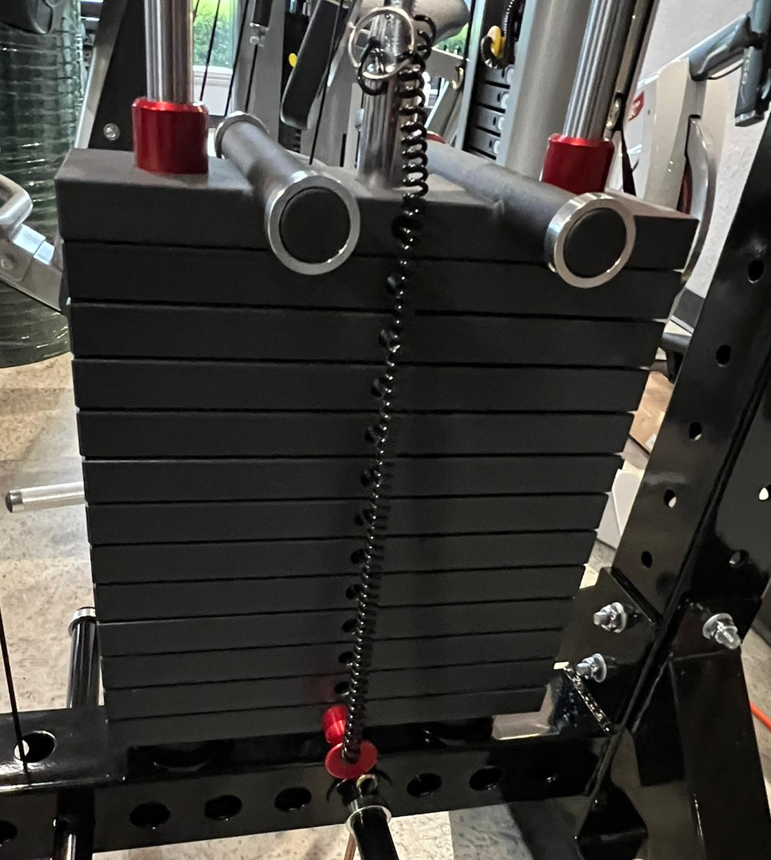 Black rubber stacked weight plate storage attachment with silver metal handles and red safety pins, mounted on gym equipment 