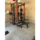 Red and black power rack with weight plates and barrels in gym setting on grey interlocking tile flooring