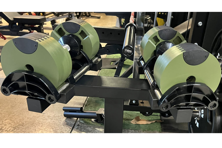 Pair of sage green adjustable dumbbells with black accents and handles on black dumbbell stand in gym setting