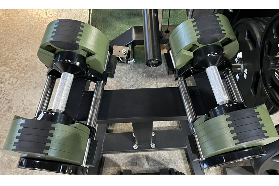 Adjustable dumbbells with sage green and black weight plates, chrome handles, on black metal weight rack, flat lay view