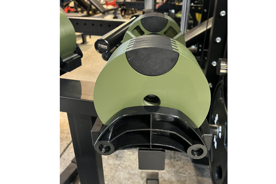 Sage green and black adjustable dumbbell weight shown from front angle in gym setting