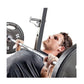 Man performing bench press exercise on black Olympic weight bench with loaded barbell and weight plates