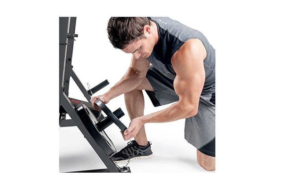 Male athlete using black and gray Olympic weight bench with adjustable seat and leg extension attachment