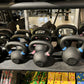 Assorted black powder-coated kettlebells with colored weight indicators arranged on gym rack shelf
