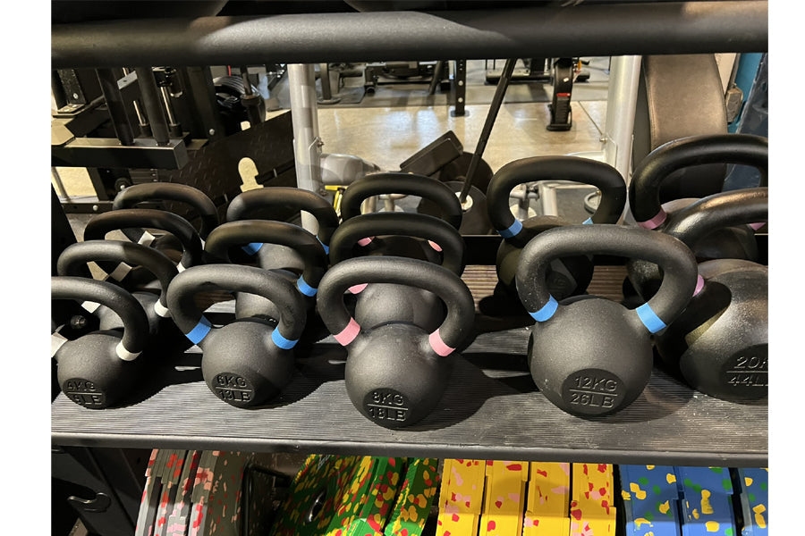 Assorted black powder-coated kettlebells with colored weight indicators arranged on gym rack shelf