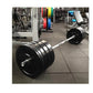 Black Olympic bumper plates loaded on chrome barbell in gym setting with colorful weight plates visible in background